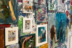 Foto einer Atelierwand bei Frau Ballerstein, zeigt mehrere Bilder an der abstrakt bemalten Wand aufgehängt.